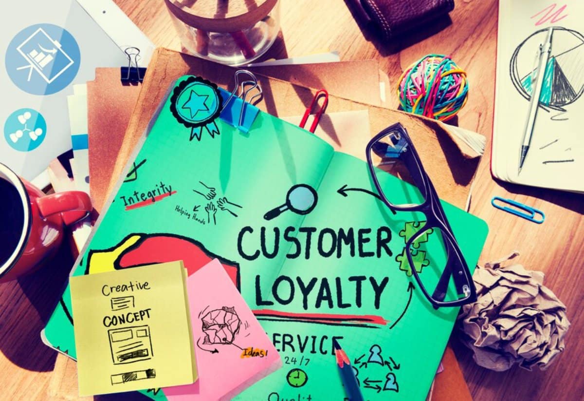 A cluttered workspace featuring notes on customer loyalty, sketches, glasses, a coffee mug, and colorful paper to emphasize creativity.